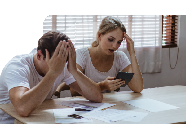 Man and woman sitting at table and looking in dispair. Man has his head in his hands. 