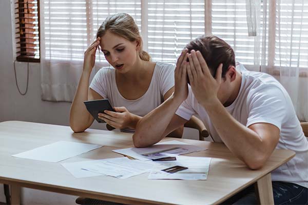 Couple sitting trying to do finances. Man has his head in his hands